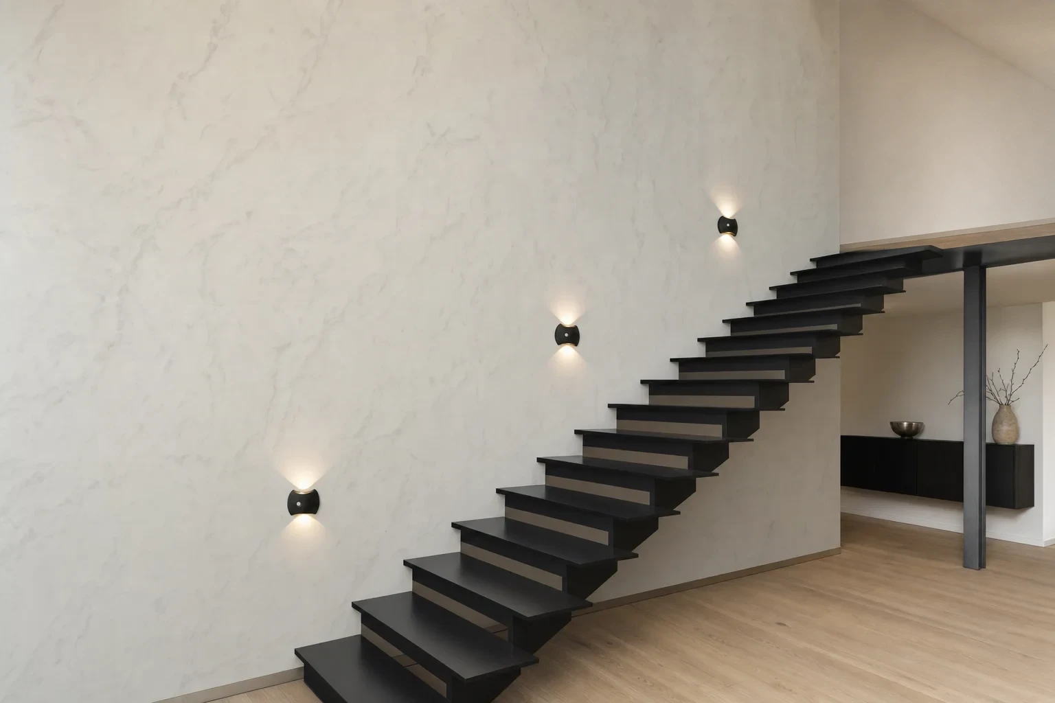Three small black Motion Sense Wall Lights glowing beside a black open staircase that rises to a quiet upstairs landing